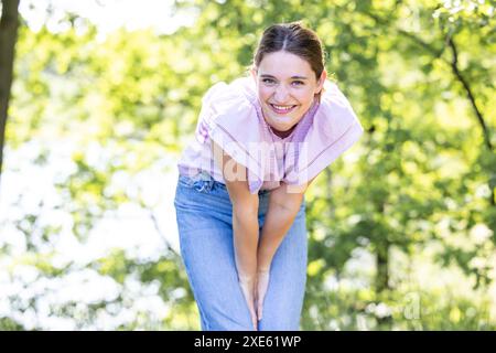 Die verspielte junge Frau lehnt sich im Park nach vorne Stockfoto