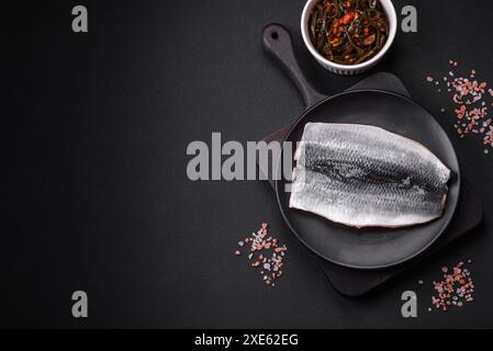 Köstliches gesalzenes Heringsfilet in Öl auf einer schwarzen Keramikplatte Stockfoto