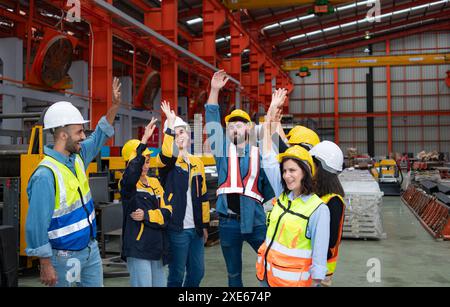 Eine Gruppe von Fabrikarbeitern in Hardhelden mit erhobenen Armen feiert den Erfolg Stockfoto