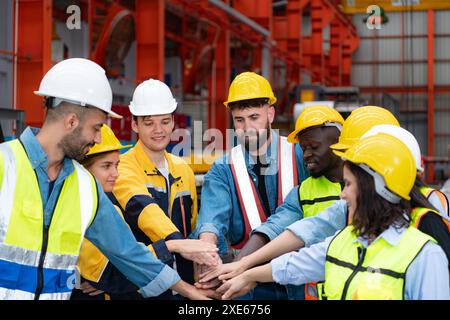 Gruppe von Fabrikarbeitern in Schutzhelmen mit gemeinsamen Händen zum Feiern des Erfolgs Stockfoto