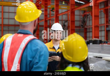 Vorgesetzter und Gruppe von Fabrikarbeitern, die Schutzhelme tragen, treffen sich kurz zusammen, bevor sie mit der Arbeit beginnen. Stockfoto