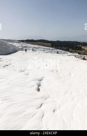 Touristen und Menschen, die an einem sonnigen Tag in der Nähe der antiken Stadt Hierapolis auf den wunderschönen weißen Travertinen von Pamukkale in Türkiye spazieren gehen. Stockfoto