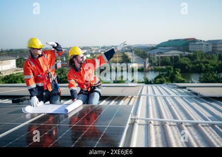 Ingenieur und Techniker, die am Sonnenkollektor auf dem Dach des Lagerhauses arbeiten, um die in Betrieb befindlichen Solarpaneele zu inspizieren Stockfoto