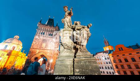 Statue des Hl. Ivo von Kermartin, beleuchtet in der Abenddämmerung mit Prager Wahrzeichen und Menschen, die im Hintergrund schlendern, Tschechische Republik Stockfoto
