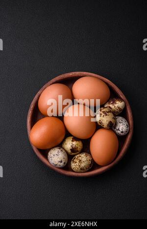 Rohes Hühnchen und Wachteleier in einer braunen Keramikschale auf dunklem Betonhintergrund Stockfoto