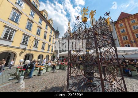 Prag, Tschechische Republik - 21. Mai 2019: Historische Ornamente verzieren den Alten kleinen Platzbrunnen im Vordergrund, während sich die Menschen in den Cafés im Freien in Prag entspannen Stockfoto