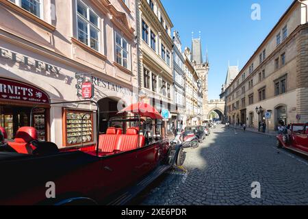 Prag, Tschechische Republik - 18. Mai 2019: Touristen schlendern entlang der Kopfsteinpflasterstraße mit roten Oldtimern, die in Prag geparkt sind und in Richtung Pulver fahren Stockfoto