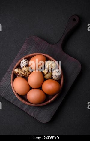 Rohes Hühnchen und Wachteleier in einer braunen Keramikschale auf dunklem Betonhintergrund Stockfoto