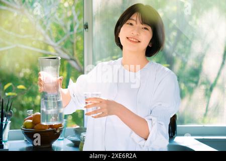 Eine junge Frau, die eine Tasse mit Wasser füllt Stockfoto