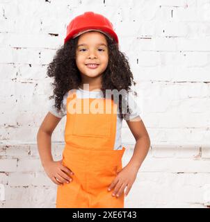 Niedliches kleines Mädchen in orangefarbener Reparaturuniform und Helm Stockfoto