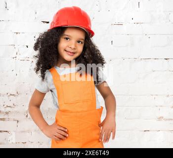 Niedliches kleines Mädchen in orangefarbener Reparaturuniform und Helm Stockfoto