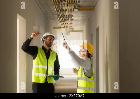 Männliche und weibliche Ingenieure, die auf der Baustelle arbeiten, überwachen die elektrische Anlage des Gebäudes. Stockfoto