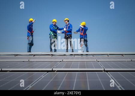 Gruppe von Ingenieuren, die auf Sonnenkollektoren stehen, mit blauem Himmel im Hintergrund Stockfoto