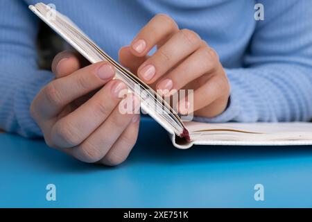 Frau hat die Hände gepflegt, stilvolle beige Nägel auf Papier Notizbuch. Die Nahaufnahme von gepflegten Nägeln der weiblichen Hand im blauen Pullover in Blau Stockfoto