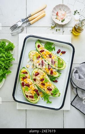 Zucchini gefüllt mit Petitim, roten Bohnen, Mais mit Basilikum und Soße, gebacken auf einem alten, zerrissenen Fliesenhintergrund. Draufsicht. Stockfoto