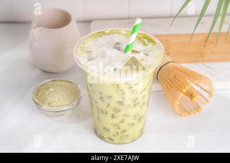 Kaltes grünes Matcha Latte Getränk. Köstlicher, eisgekühlter Matcha-grüner Tee gemischt mit Eiswürfeln und Schlagsahne in Latte-Glas auf weißem Tischhintergrund Stockfoto