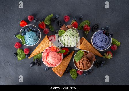 Buntes helles Eis auf Schüsseln, mit Waffelkegeln und Beeren, auf schwarzem Hintergrund. Verschiedene Eisportionen mit verschiedenen Aromen und frischen Zutaten Stockfoto