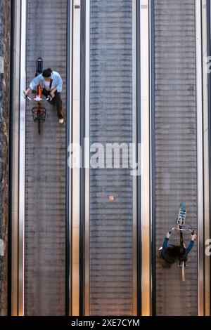 Auf zwei Frauen, die ihre Fahrräder auf einen Reisenden schieben, der die unterirdische Fahrradparkanlage vor dem Amsterdamer Hauptbahnhof in den Niederlanden verlässt. Stockfoto