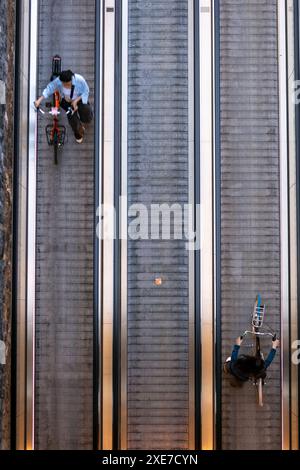 Ein Blick von oben auf zwei Frauen, die ihre Fahrräder auf einen Reisenden schieben, der die unterirdische Fahrradparkhalle vor dem Amsterdamer Hauptbahnhof in den Niederlanden verlässt. Stockfoto