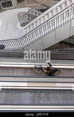 Eine Frau schiebt ihr Fahrrad an einem Reisenden vorbei und verlässt die unterirdische Fahrradparkanlage vor dem Amsterdamer Hauptbahnhof in den Niederlanden. Stockfoto