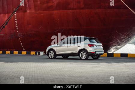 Silver SEAT Arona parkte am Rumpf eines riesigen Schiffes in einem Hafen. Dreiviertel-Rückansicht der spanischen Fließheck-Überkreuzung Stockfoto