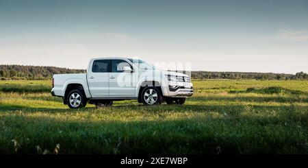 Weißer Volkswagen Amarok auf grüner Wiese. Vordere Dreiviertelansicht eines VW-Pickup-Multimeters mit Doppelkabine auf einem Feld. Stockfoto