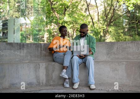 Interessiertes Paar schwarze Studenten Mädchen und Mann sitzen mit Laptop auf dem College Campus und reden Brainstorming. Stockfoto