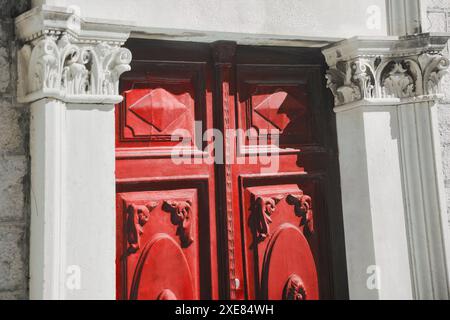 Große rote Tür mit komplizierten Schnitzereien und einem Messingknauf. Die Tür ist mit einem Design und Säulen dekoriert Stockfoto