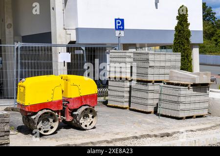 Gelb-rote Maschine zum Verdichten von Boden und Straßenfliesen, die auf Holzpaletten auf einer Baustelle gelagert werden. Stockfoto