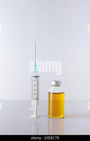 Spritze mit Nadel und injizierbarer Arzneimittelflasche in aufrechter Position. Vertikal. Weißer Hintergrund. Stockfoto