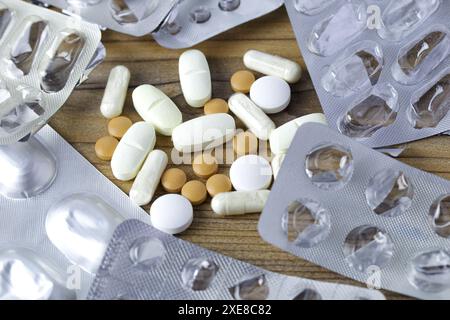 Tabletten und Arzneimittelkapseln umgeben von leeren Blisterpackungen auf einem Holztisch. Drogenübernutzung oder Suchtkonzeptionsidee. Stockfoto