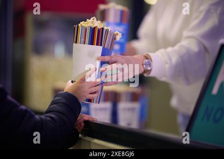 Ein Verkäufer steht vor dem Kino und hält frisches Popcorn, um es an Kinobesucher zu verkaufen, bevor sie das Kino betreten Stockfoto