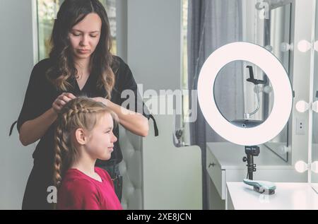 Die Friseurin webt im Schönheitssalon eine Flechtflechte zu einem jungen Mädchen Stockfoto