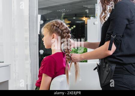 Die Friseurin webt im Schönheitssalon eine Flechtflechte zu einem jungen Mädchen Stockfoto