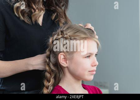 Die Friseurin webt im Schönheitssalon eine Flechtflechte zu einem jungen Mädchen Stockfoto