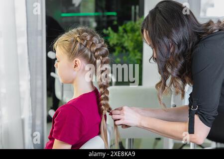 Die Friseurin webt im Schönheitssalon eine Flechtflechte zu einem jungen Mädchen Stockfoto