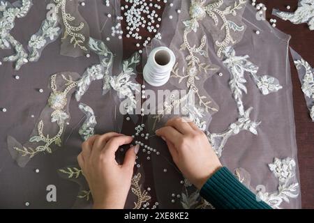 Nahaufnahme weiblicher Hände einer Schneiderin, die Hochzeitskleider mit Perlen und Spitze im Atelier nähen Stockfoto