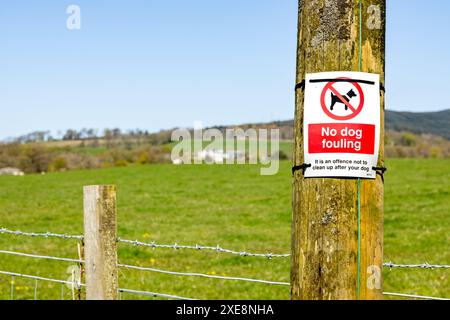 Auf dem Land, an einem verwitterten Telegrafenmast festgebunden, mit der Nachricht: Kein Hund fouling, es ist eine Straftat, nicht hinter deinem Hund aufzuräumen. Stockfoto