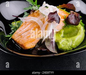 Nahaufnahme von gegrilltem Lachsfilet mit grünem Rucolasprossen und Avocado-Püree auf einem Teller. Stockfoto