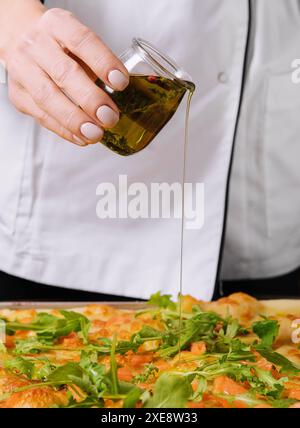 Koch gießt Olivenöl auf Pizza Stockfoto