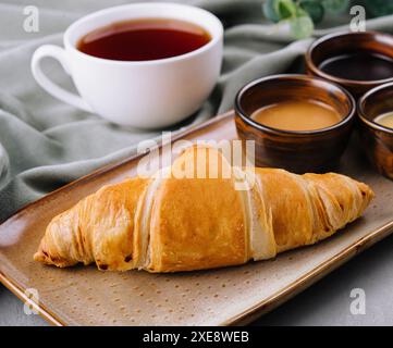 Frische französische Croissants mit Schokolade auf Teller, Heidelbeermarmelade, Honig und Tee Stockfoto