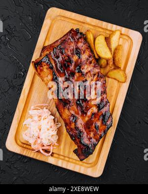 Schweinerippchen, serviert auf Schneidebrett und Kartoffelscheiben Stockfoto