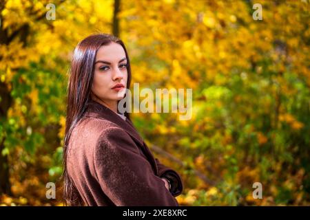 Junge schöne Frau in braunem Mantel im Park im Herbst Stockfoto