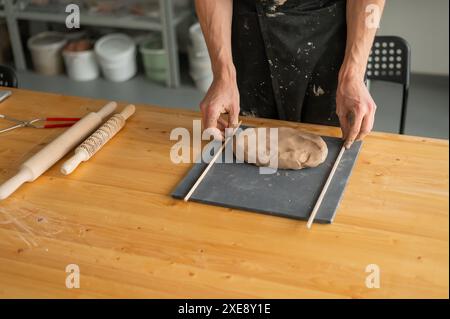 Nahaufnahme von Töpferhänden, die Ton ausrollen. Stockfoto