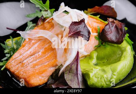 Nahaufnahme von gegrilltem Lachsfilet mit grünem Rucolasprossen und Avocado-Püree auf einem Teller. Stockfoto