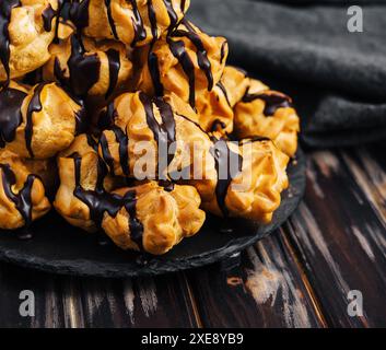 Profiterolen mit Schokoladencreme auf schwarzer Platte Stockfoto