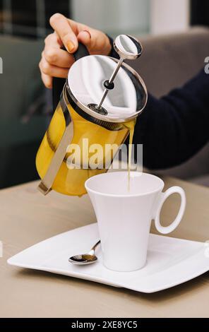 Eine Frau gießt Sanddorntee aus einer Teekanne in eine Tasse Stockfoto