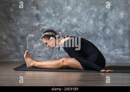 Eine Frau mittleren Alters führt eine Übung durch, um die Muskeln von Rücken und Beinen zu dehnen, lehnt sich aus einer Sitzposition nach vorne, trainiert in Sportbekleidung o Stockfoto