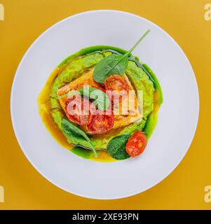 Lachssteak mit Avocadopüree, dekoriert mit Basilikumblättern und Kirschtomaten Stockfoto