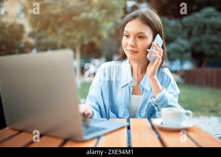 Frau, die Laptop und Telefon benutzt, während sie am Tisch im Freien sitzt Stockfoto
